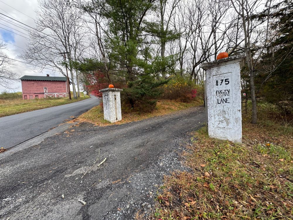 The farm entrance at 175 Cherry Lane: two white gateposts, one marked 175 Cherry Lane, with a red barn and evergreens beyond